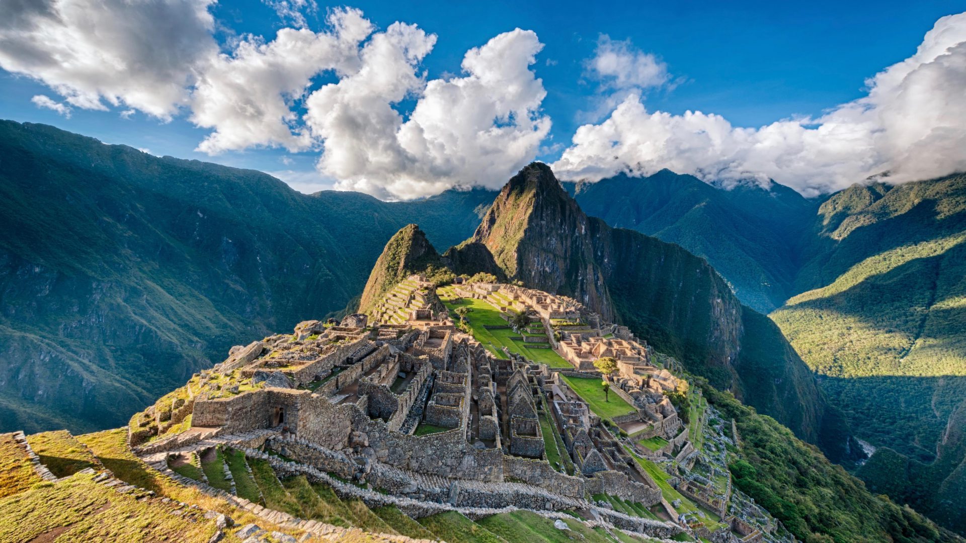 A view facing Machu Pichu in the Peruvian Andes with a blue sky and pearly white clouds