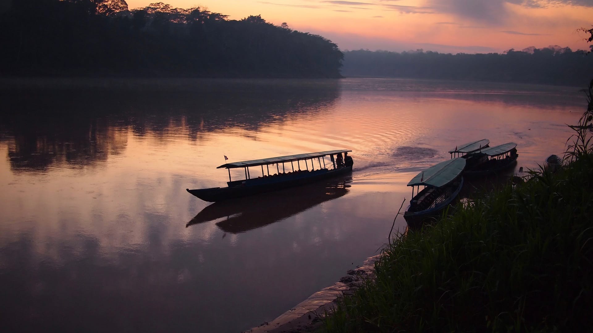 A boat navigating the Tambopata river during sunrise in the Amazon rainforest in Peru.